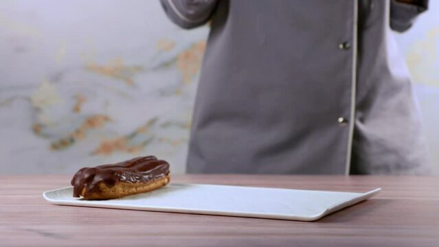 French dessert eclair with dark chocolate glaze. Woman putting baked French eclairs on a plate.