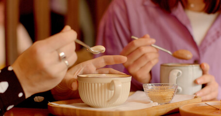 Close-up of feminine hands delicately swirling coffee spoon through frothy foam cappuccino or cocoa. Hands with elegant rings add touch of sophistication to scene, embodying grace of lady's touch. 