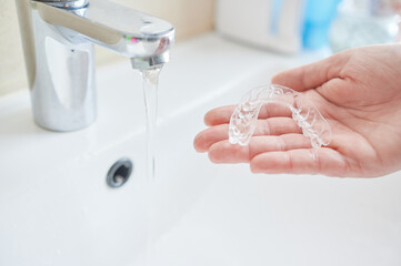 Unrecognizable woman's hand holding invisible orthodontics to clean it with tap water at the...