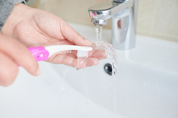 Unrecognizable woman washing  invisible orthodontics with a teeth brush and tap water at the...