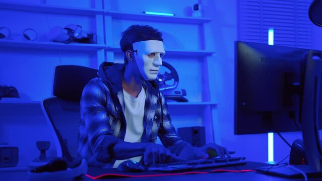 hacker wearing a white mask is using a computer to steal confidential information.Concepts: computer crime, burglary, business security on computer networks
