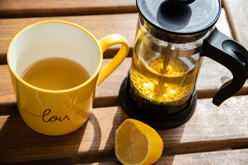 Teapot (French press) with half lemon and teapot at wooden table on the balcony, morning tea time, aromatic aromatherapy fresh and herbal, organic tea from farm. In background neighborhood buildings
