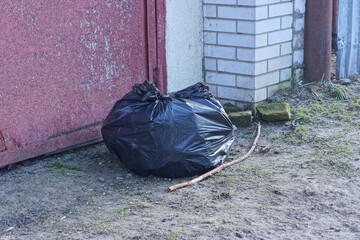 one black plastic bag with garbage stands on the gray ground on the street