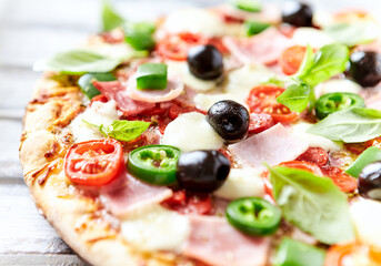 Pizza with ham, mozzarella cheese, cherry tomatoes, green and jalapeno pepper, black olives and fresh basil. Bright background. Close up.	
