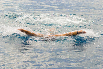 Open water swimming takes place in open bodies of water such as open oceans, lakes and rivers. A man swims in sea water, the hands of a swimmer. Sicily, Italy. Sports recreation