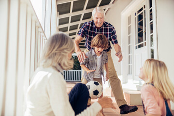 Grandparents and grandchildren having fun with a soccer ball on house porch