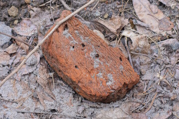 a piece of one old dirty brown red brick lies on gray sand in the street