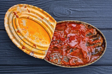 one open almina oval tin can with sardine fish in tomato sauce lies on a black wooden table
