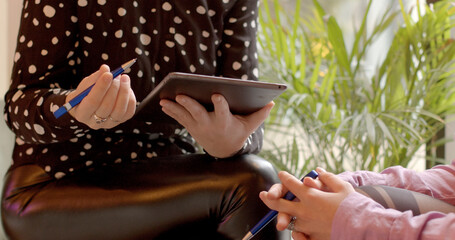 Close-up of two woman with tablet talking during informal Work Meeting: Two Colleagues Discussing Business Matters in Relaxed Setting. Casual workplace interactions. No face people, hands gesturing.