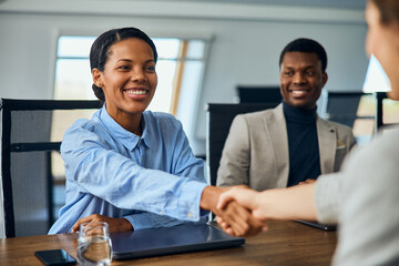 Smiling African businesswoman doing a handshake with a female client.