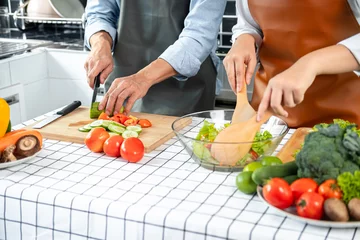 Fotobehang Asian romantic couple slice cucumber and tomato with knife on chopping board and holding ladle to mixing © Freedomz