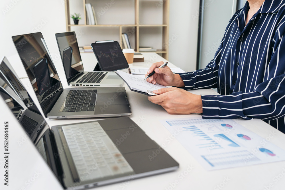 Poster Business man trader checking statistics graph on laptop and statistics data on document to analyze about stock market