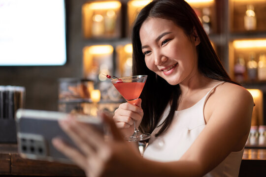 Beautiful woman is holding cocktail and using smartphone to selfie during having enjoy to relaxing while sitting alone