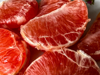 Pieces of peeled red grapefruits lying on a plate close-up