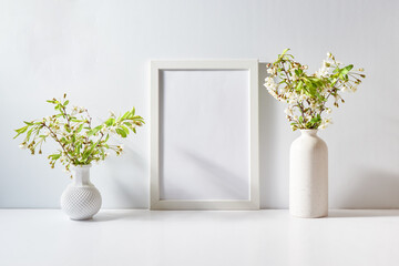 Mockup with a white frame and spring flowers in a vase on a light background. Empty poster frame...