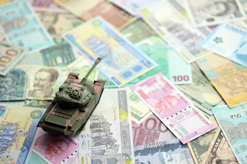 Small green tank on many banknotes of different currency. Background of war funding or spend money to defense close up