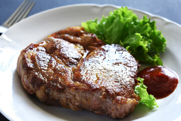 Pork steak with salad and sauce in a white plate.
