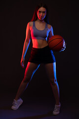 A beautiful slender girl athlete in shorts and a top plays basketball.