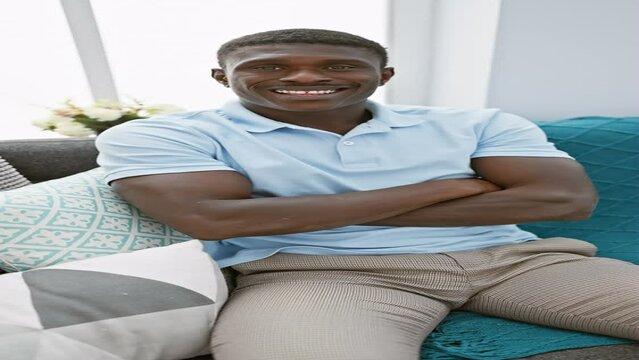 Handsome adult black man smiling and sitting with arms crossed in a modern living room.