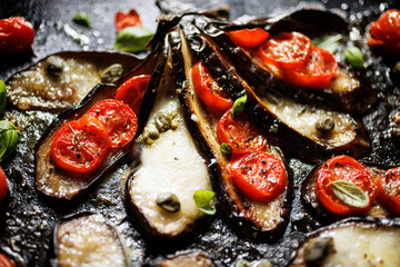 Close up of roasted eggplant in the fan shape stuffed with cherry tomatoes and mozzarella cheese sprinkle herbs on a d black background, focus on the middle