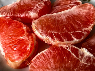 Pieces of peeled red grapefruits lying on a plate close-up