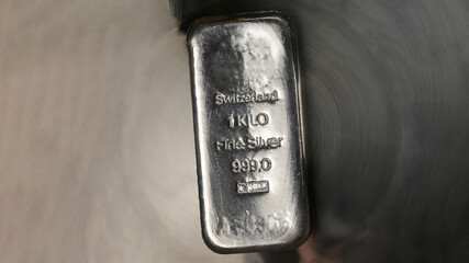 Cast silver bar weighing one kilogram on an abstract metal background.