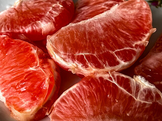 Pieces of peeled red grapefruits lying on a plate close-up