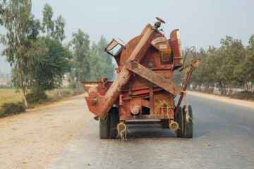 Fototapeta premium old rusty rice thresher on road with tractor