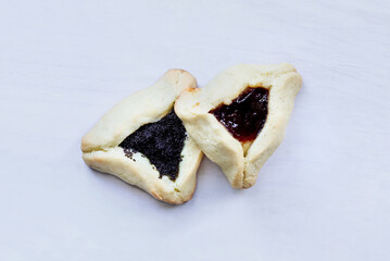 Two traditional hamantaschen cookies filled with mohn paste (poppy seed paste) and plum jam for the Jewish festival of Purim over a white wood table.