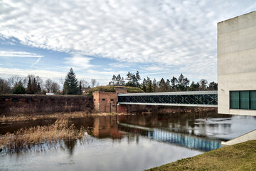 modern building, pedestrian bridge and historic defensive walls over the Warta River in Poznan - obrazy, fototapety, plakaty