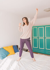 Happy young excited woman jumping on the bed at home