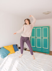 Happy young excited woman jumping on the bed at home - 752513648