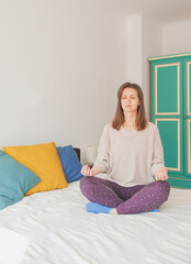 Young beautiful woman meditates sitting on the bed at home
