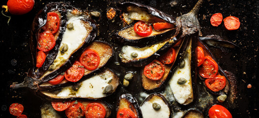 Baked eggplants stuffed with cherry tomatoes and mozzarella cheese on a black background, close up view