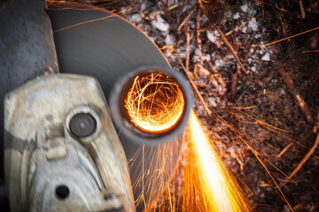 Angle grinder radial machine cutting steel tube with bright sparks stream, close up