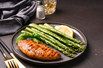 Baked asparagus and grilled chicken fillet in a plate on a dark background