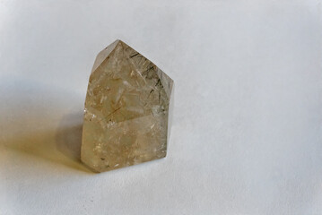 Rutilated quartz crystal in golden tones with reflection on white background