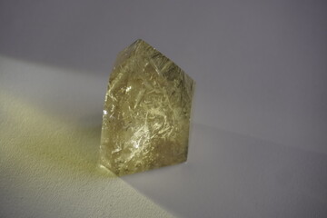 Rutilated quartz crystal in golden tones with yellow reflection on white background