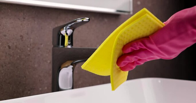 cleaning service and chores. hand with rubber glove and sponge cleaning the bathroom sink faucet