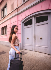 Fototapeta na wymiar Stylish travel and urban exploration: vibrant young latina brunette with fashion look and pink suitcase exploring city historic district and downtown