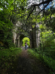 A lone wanderer follows an enchanted path beneath the arch of Overtoun Bridge