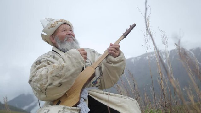 An old man in the mountains tunes and plays the Kyrgyz musical instrument komuz