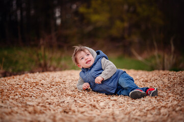 A little boy lies in a bed of wood chips, his joy and playfulness captured in a natural outdoor setting, with a backdrop of trees