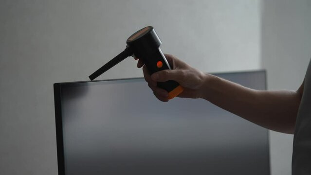 Close-up cropped shot of unrecognizable man cleaning monitor screen using pneumatic cleaner, compressed air bottle. Male blows dust off modern monitor during general cleaning of house, slow motion.