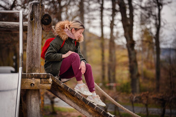 A woman sits contemplatively on a wooden beam at a playground, her casual pose and soft focus backdrop evoke a sense of peaceful reflection