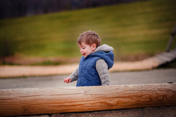 A small boy laughs with delight while playing on a wooden structure at a playground, the embodiment of childhood merriment and unbridled happiness