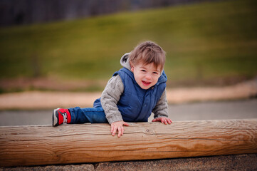 : A toddler experiences the challenge of climbing over a wooden beam, a candid snapshot of the learning and growth that comes with play