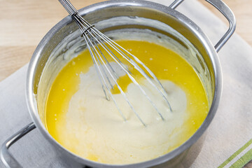 Melted butter with milk in a saucepan. The process of preparing a dish using a whisk