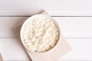 Homemade crumbly cottage cheese in a white bowl on a white table