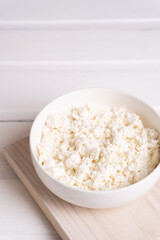 Homemade crumbly cottage cheese in a white bowl on a white table